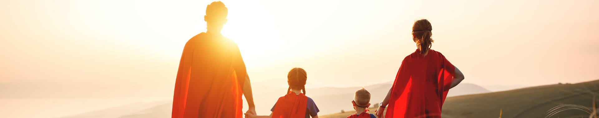 image of dad, two kids, and mom in superhero costumes with their back to the camera looking at the sunset